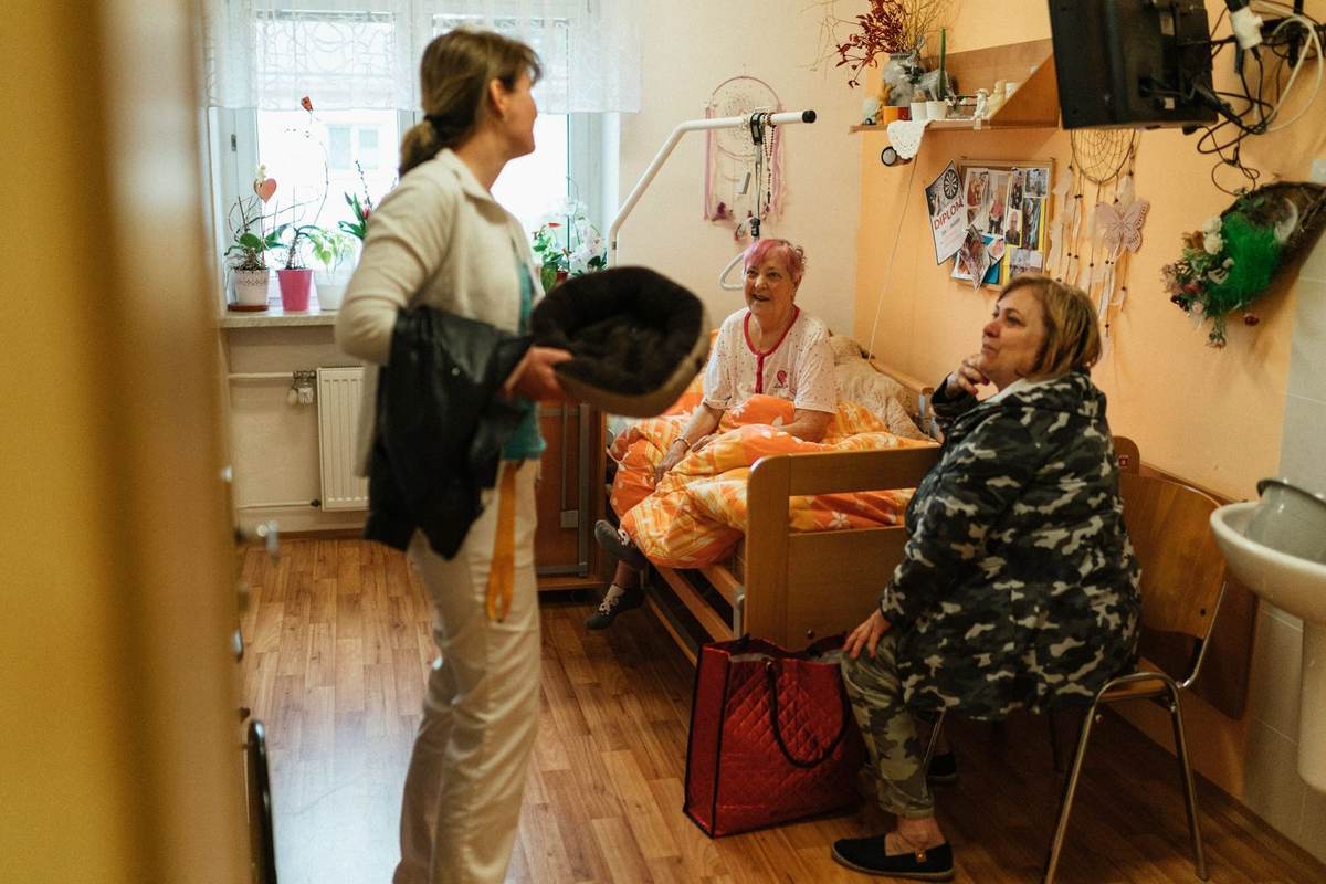 Two older women talking with a caregiver in a bright care-home lounge.